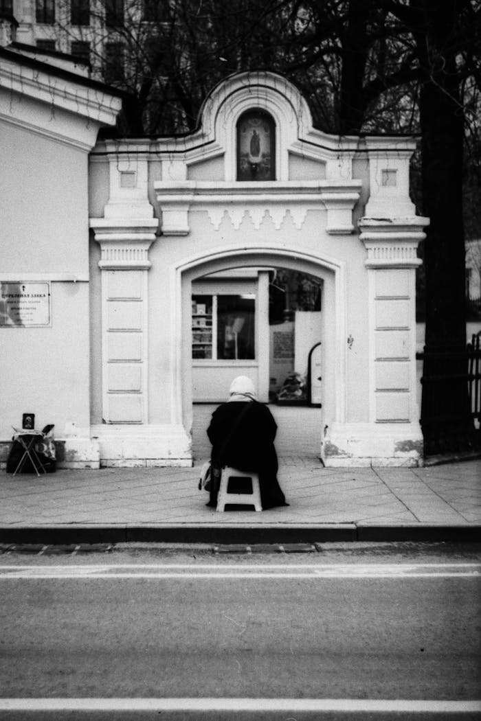 gallery-6 A lone person sits in front of a classic architectural doorway, creating a serene urban scene.