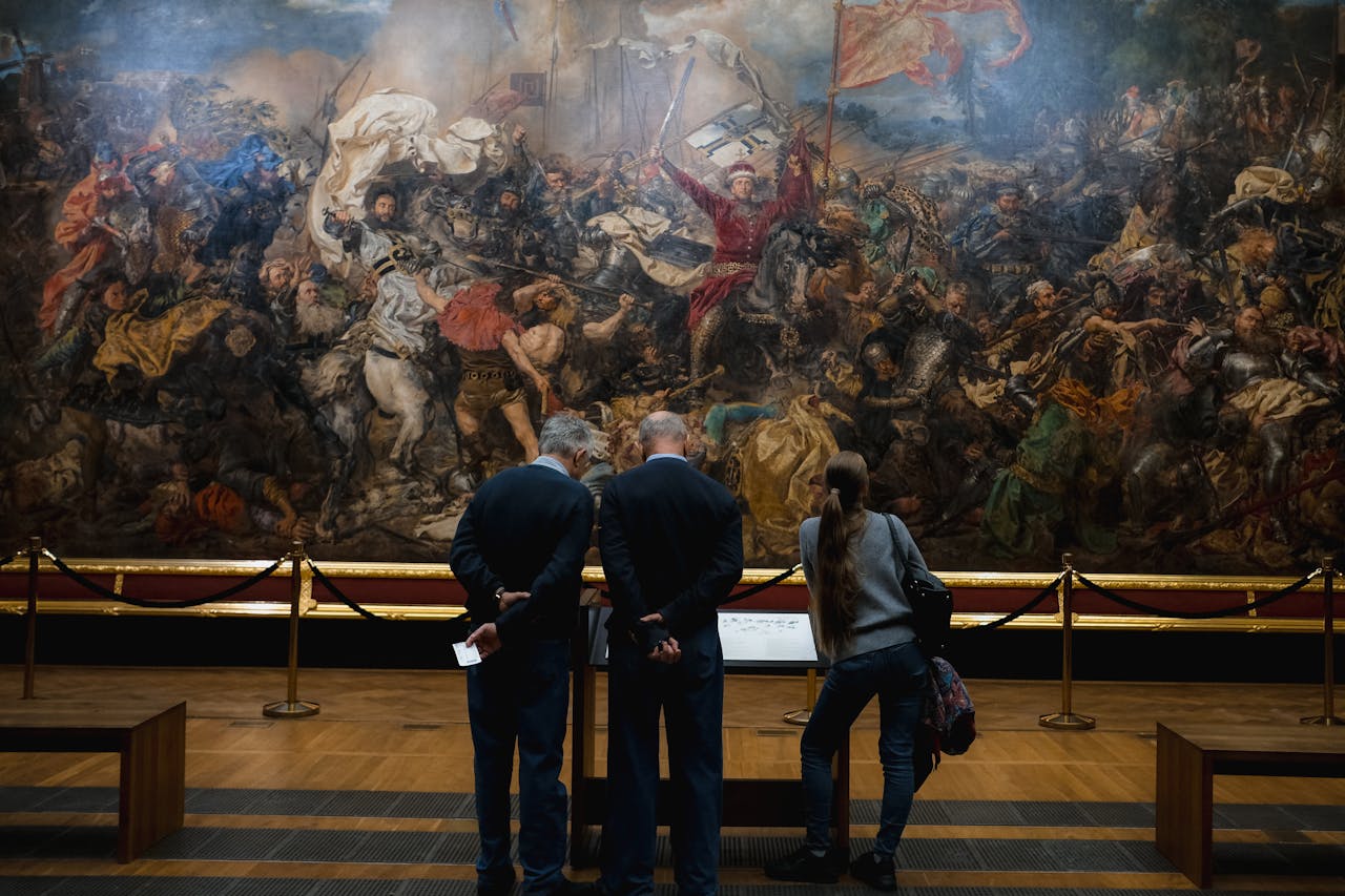 services-04 People viewing a large, detailed historical battle painting in a museum setting.