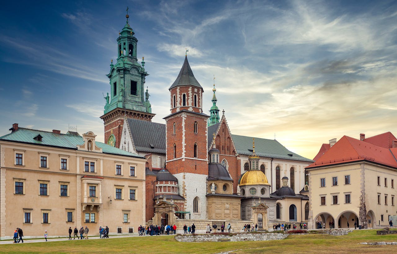 services-01 Traditional aged buildings and ancient Wawel Cathedral with various towers located on hill in Krakow against cloudy blue sky at sunset