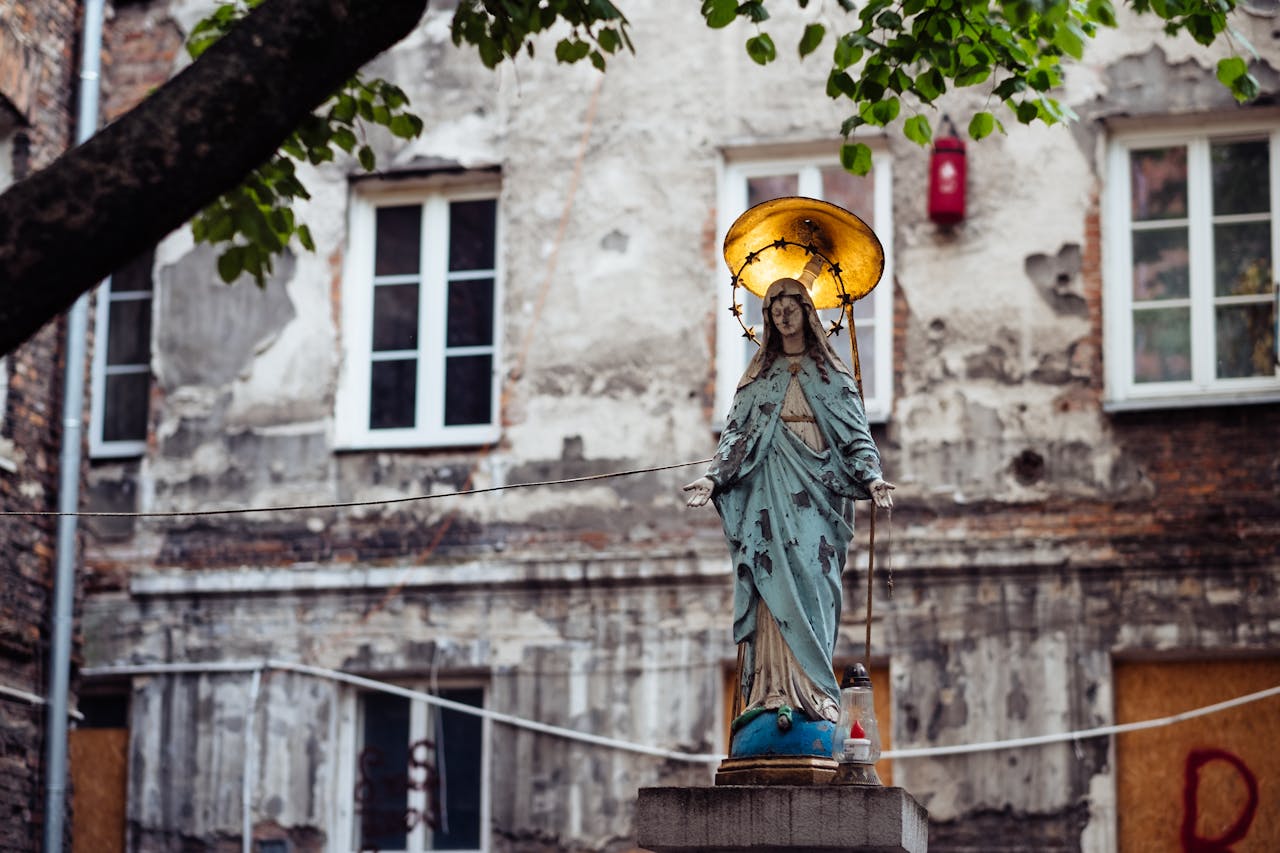 hero-img-01 Statue of Virgin Mary with halo against Warsaw's aged buildings, symbolizing faith.